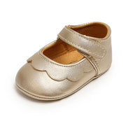 Gold baby shoe with scalloped edge on a white background