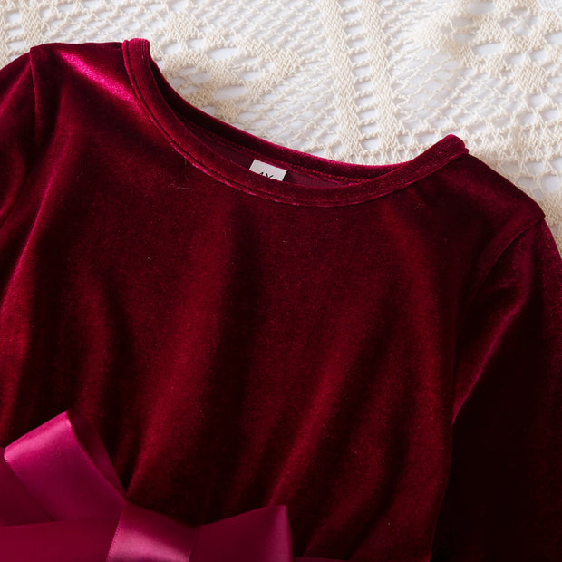 Close-up of a burgundy velvet garment with a bow on a textured beige surface
