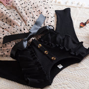 Black ribbed romper with ruffles and buttons on a textured surface