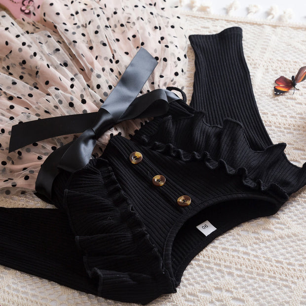 Black ribbed romper with ruffles and buttons on a textured surface