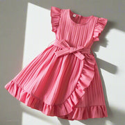 Pink dress with ruffled details on a textured surface with decorative items.