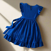 Blue dress with ruffled sleeves and hem on a textured surface with decorative items.