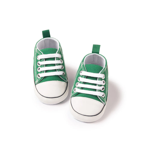 Pair of green baby sneakers with white soles on a white background