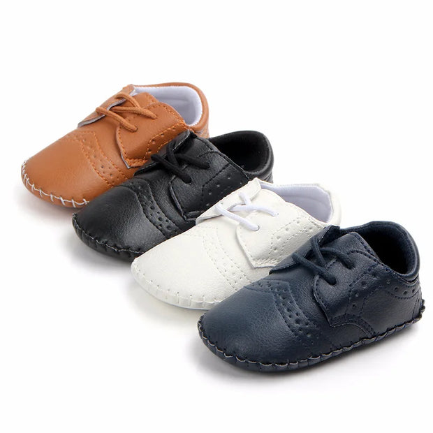 Set of four baby shoes in brown, black, white, and navy on a white background