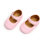 Pair of pink baby shoes with a scalloped edge on a white background