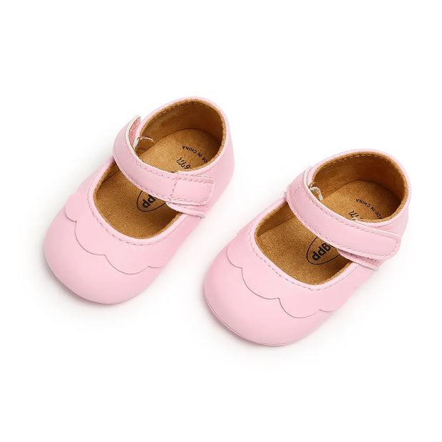 Pair of pink baby shoes with a scalloped edge on a white background