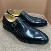 Pair of black dress shoes with a buckle on a textured surface