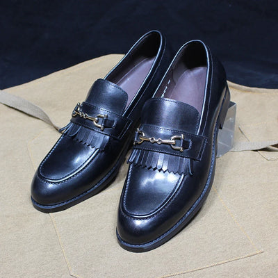 Pair of black leather loafers with gold buckles on a beige surface.