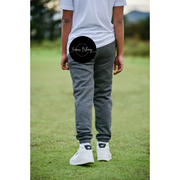 Person wearing gray sweatpants and white sneakers on a grassy field with a blurred background