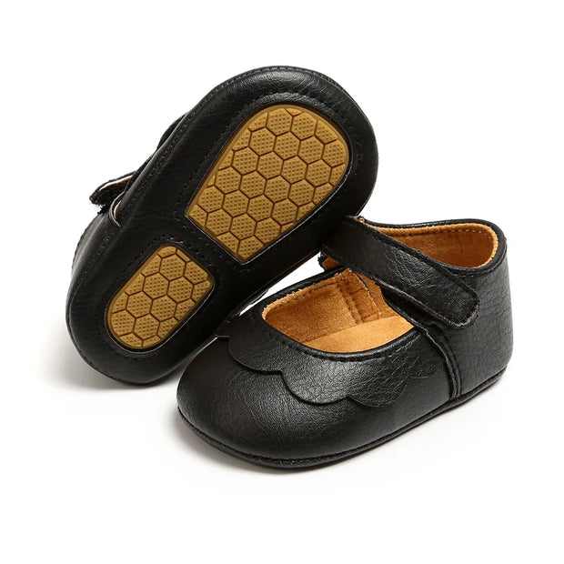 Pair of black baby shoes with brown soles on a white background