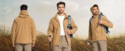 Three men wearing brown jackets in a field with backpacks and walking sticks.