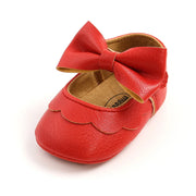 Red leather baby shoe with a large bow on a white background