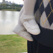 White shoes with a scalloped edge worn by a person standing near a body of water.