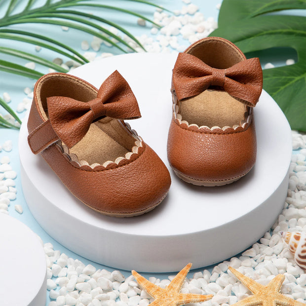 Pair of brown leather baby shoes with bows on a white platform with decorative elements.