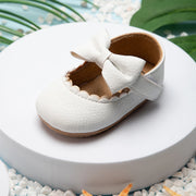White baby shoe with a bow on a white surface