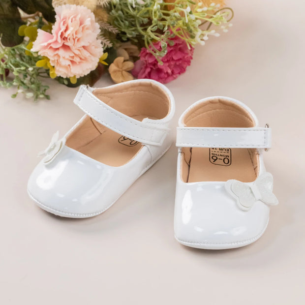 White baby shoes with a bow on a light background with flowers.