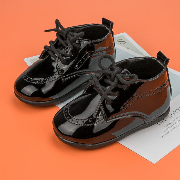 Pair of black patent leather shoes with laces on an orange background