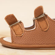 Brown baby sandal with velcro straps on a beige background