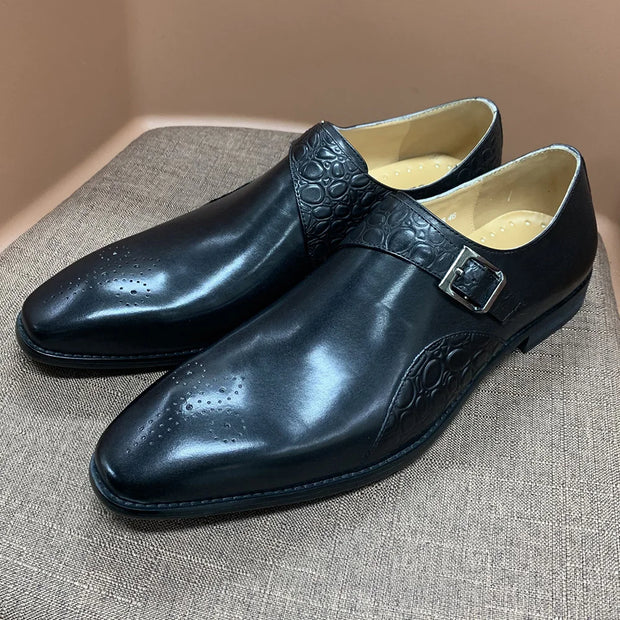Pair of black dress shoes with a buckle on a textured surface