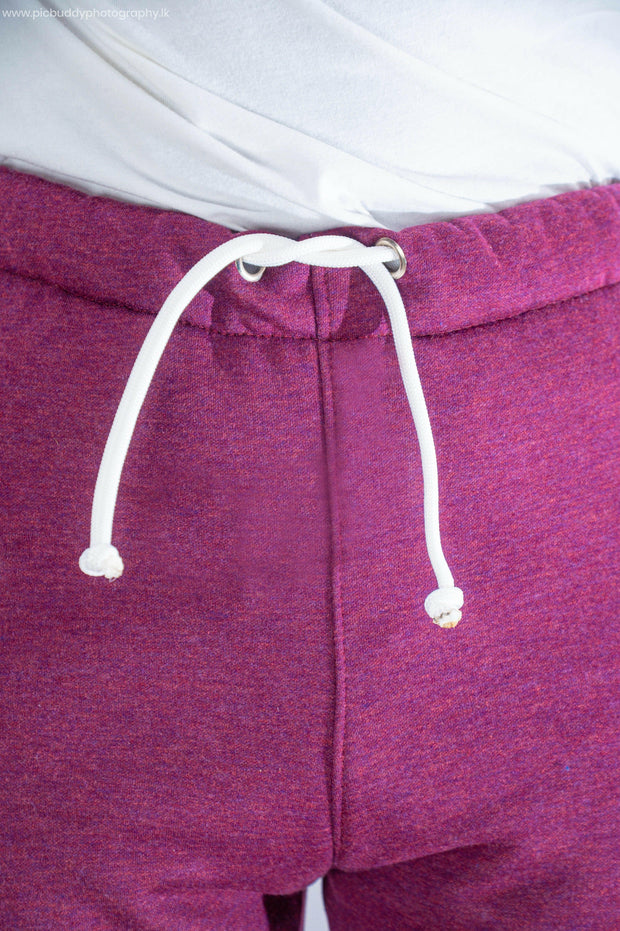 Close-up of purple sweatpants with a white drawstring on a plain background