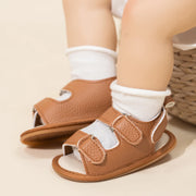 Brown baby sandals worn with white socks on a neutral background