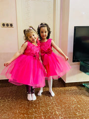 Two young girls in pink dresses standing indoors.