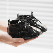 Black shiny shoes held in a hand against a light background