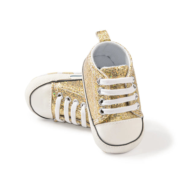 Gold glitter baby sneakers with white laces on a white background