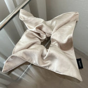 Beige silk scarf with a brand tag on a reflective surface