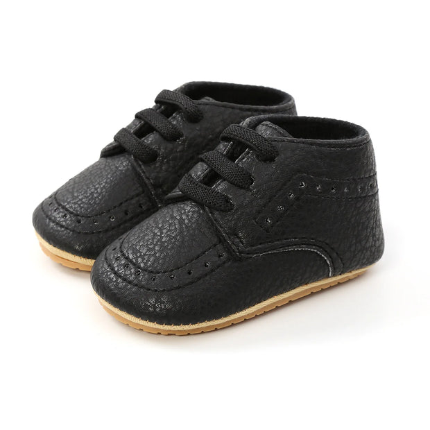 Pair of black baby shoes with brown soles on a white background