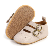 Beige baby shoes with gold buckles on a white background