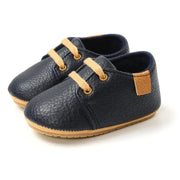 Pair of navy blue children's shoes with tan laces and soles on a white background