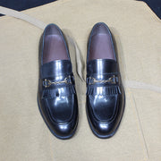 Pair of black loafers with gold buckles on a beige surface