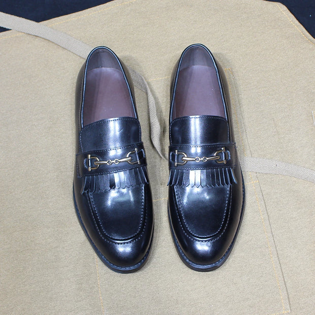 Pair of black loafers with gold buckles on a beige surface