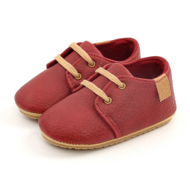Red baby shoes with beige laces and soles on a white background