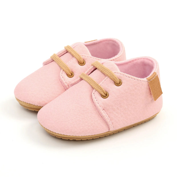 Pink baby shoes with brown accents on a white background