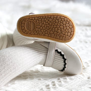 White baby shoes with brown soles on a white textured surface