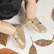 Gold glittery shoes worn by a child on a white background with brown leaves.