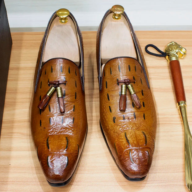 Pair of brown leather loafers with decorative tassels on a wooden surface.