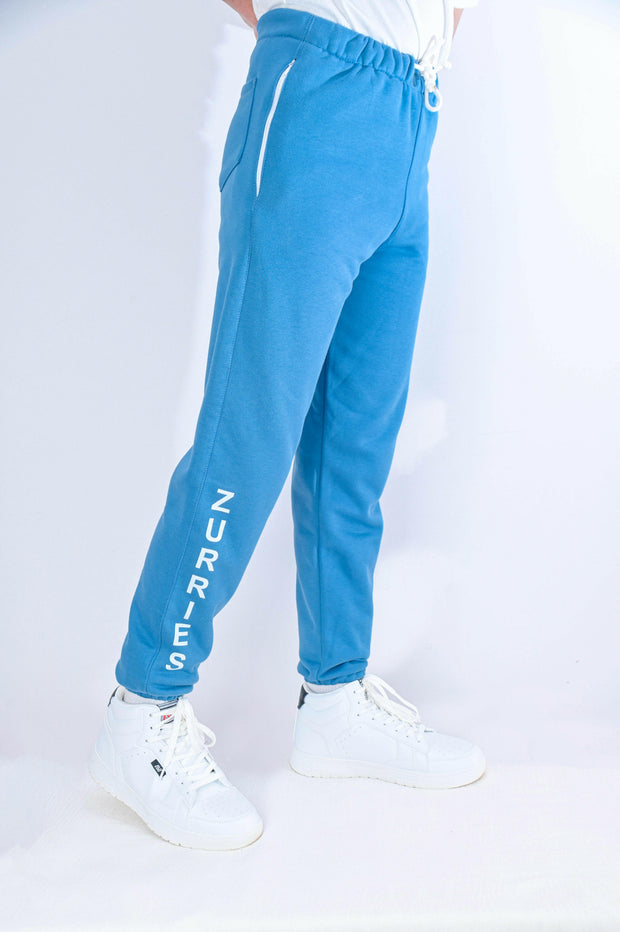 Blue jogger pants with 'Nuries' branding worn by a person on a white background