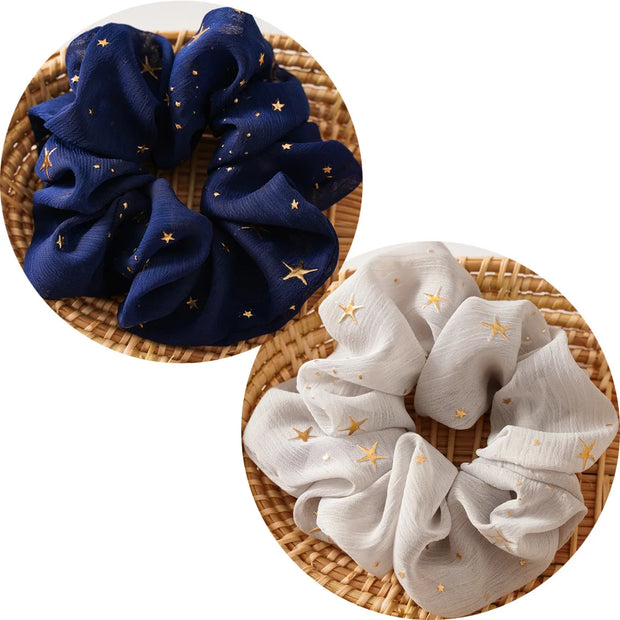 Two scrunchies, one blue and one white, with star patterns on a woven surface.