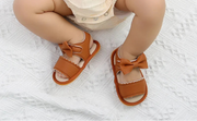 Brown sandals with bows worn by a child on a white textured surface