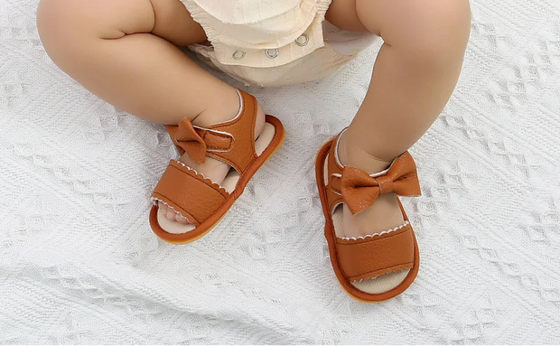 Brown sandals with bows worn by a child on a white textured surface