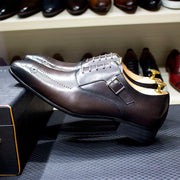 Silver dress shoe with gold accents on a textured surface, with other shoes in the background.
