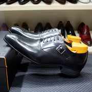 Black leather dress shoes with a wooden shoe tree on a textured surface.