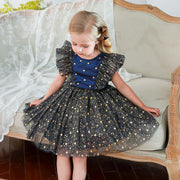 Young girl in a black star-patterned dress sitting on a decorative chair.