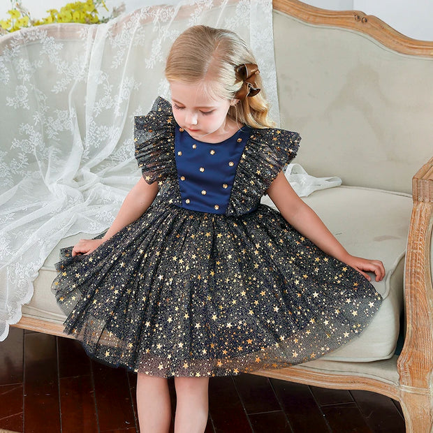 Young girl in a black star-patterned dress sitting on a decorative chair.