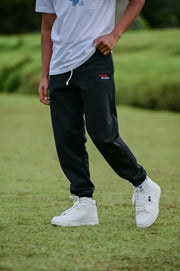 Person wearing black pants with a logo and white sneakers on grass