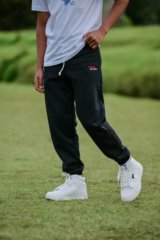 Person wearing black pants with a logo and white sneakers on grass