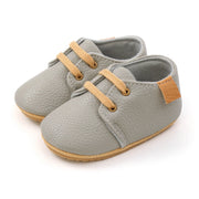 Pair of gray baby shoes with tan laces and soles on a white background